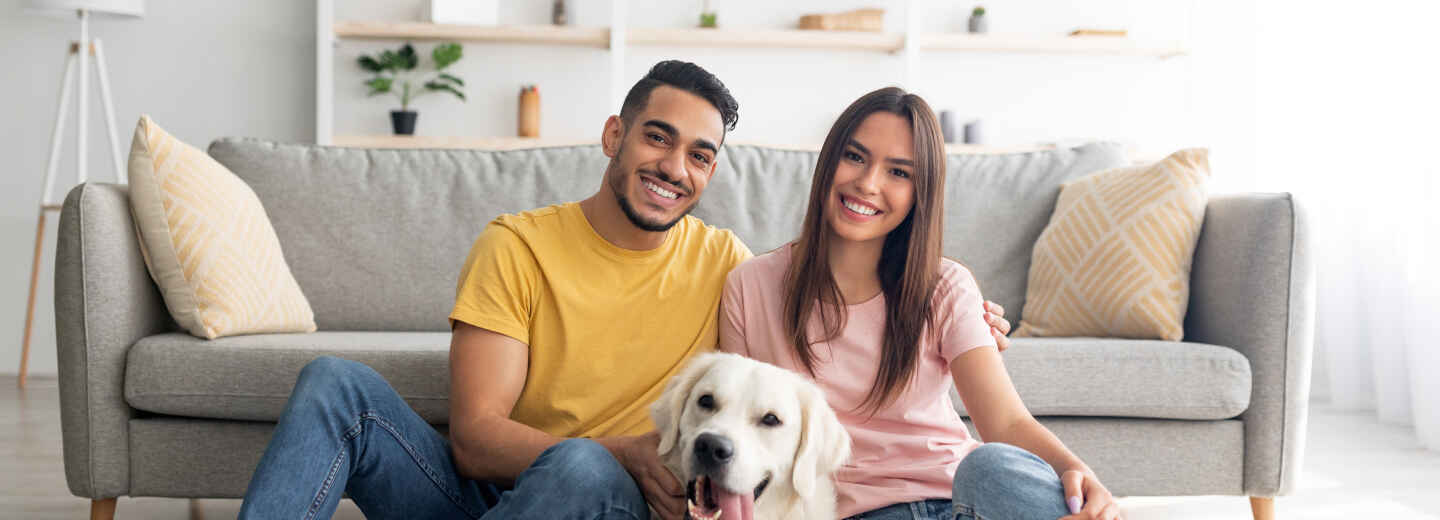 Couple on the floor in front of a couch playing with their dog