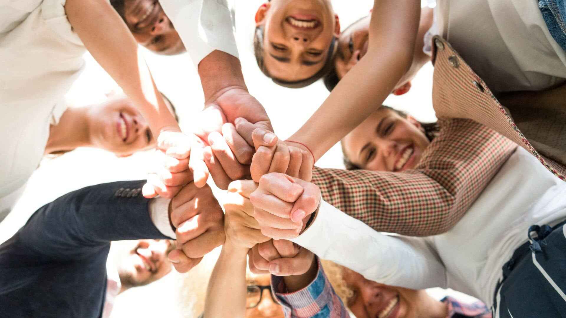Team members putting their hands in the center of a group circle from below