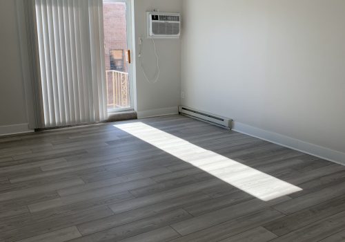 An air conditioning unit sits on a wooden floor in a room with white walls and wood floors
