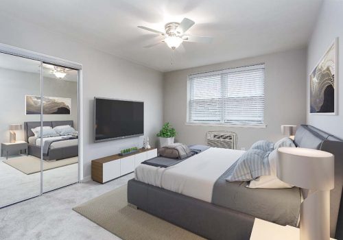 Light grey walls & carpet in bedroom. Mirror closet doors, mounted TV, & window. With A/C unit & fan