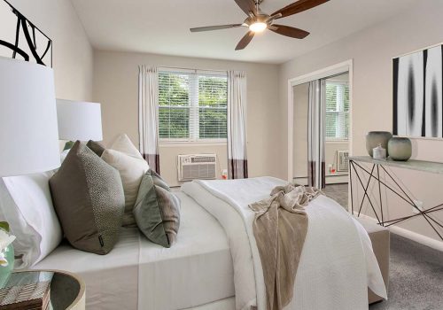 Fully furnished tan bedroom with a ceiling fan, lamps, and window at Westgate Arms apartments