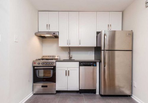 Updated kitchen with stainless steel appliances, grey tile flooring, and white shaker cabinetry.